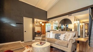 A modern living room with a sofa, coffee table, and a dining area visible in the background. - Sunlit Designer Home with Sunroom (Garland)