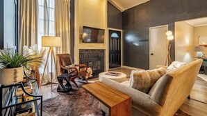 A living room with a fireplace, a sofa, a coffee table, a TV, and a lamp. - Sunlit Designer Home with Sunroom (Garland)