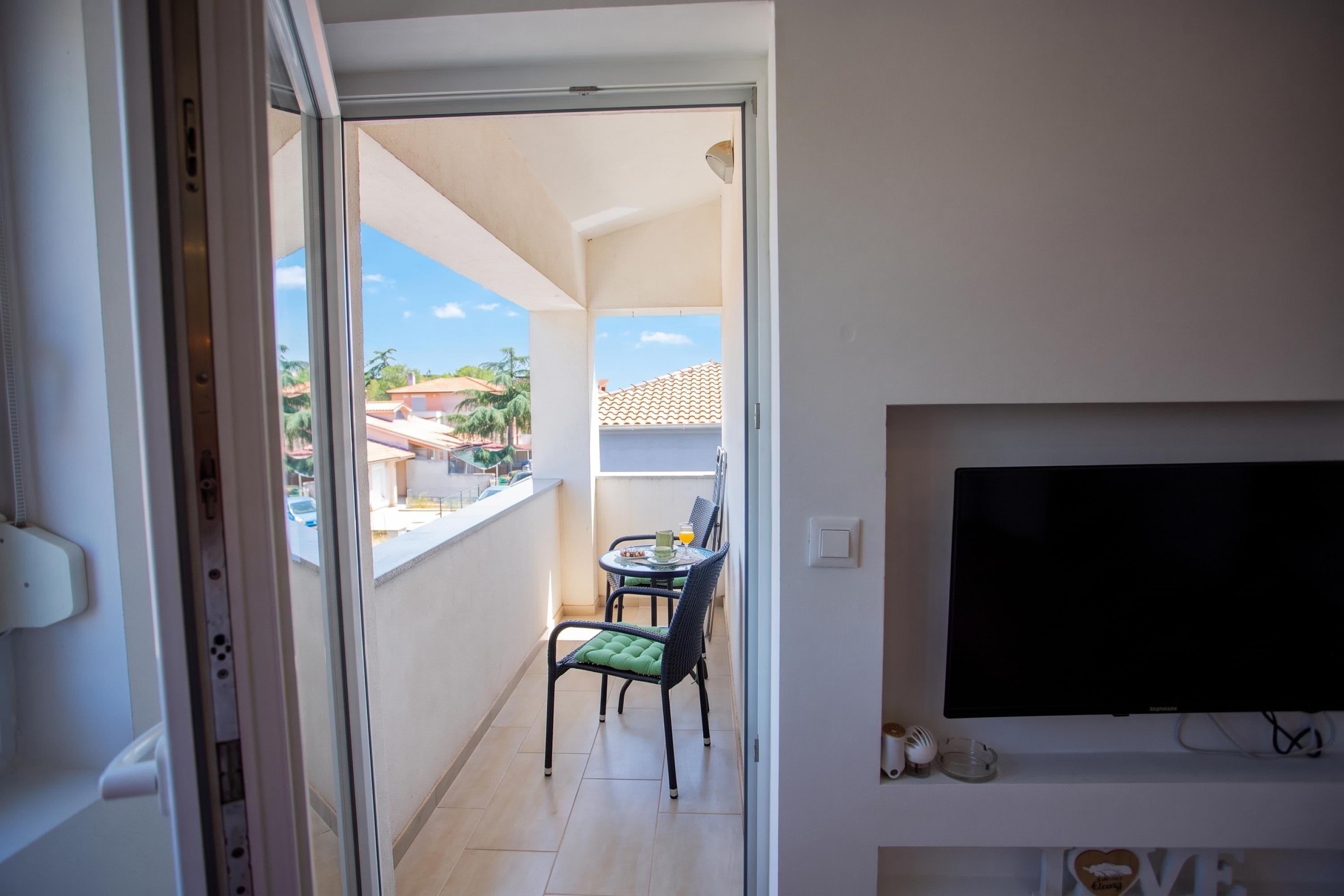 A balcony with a table and chairs, a TV mounted on the wall, and a clear view of the neighborhood.