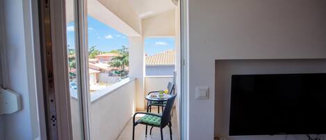 A balcony with a table and chairs, a TV mounted on the wall, and a clear view of the neighborhood.