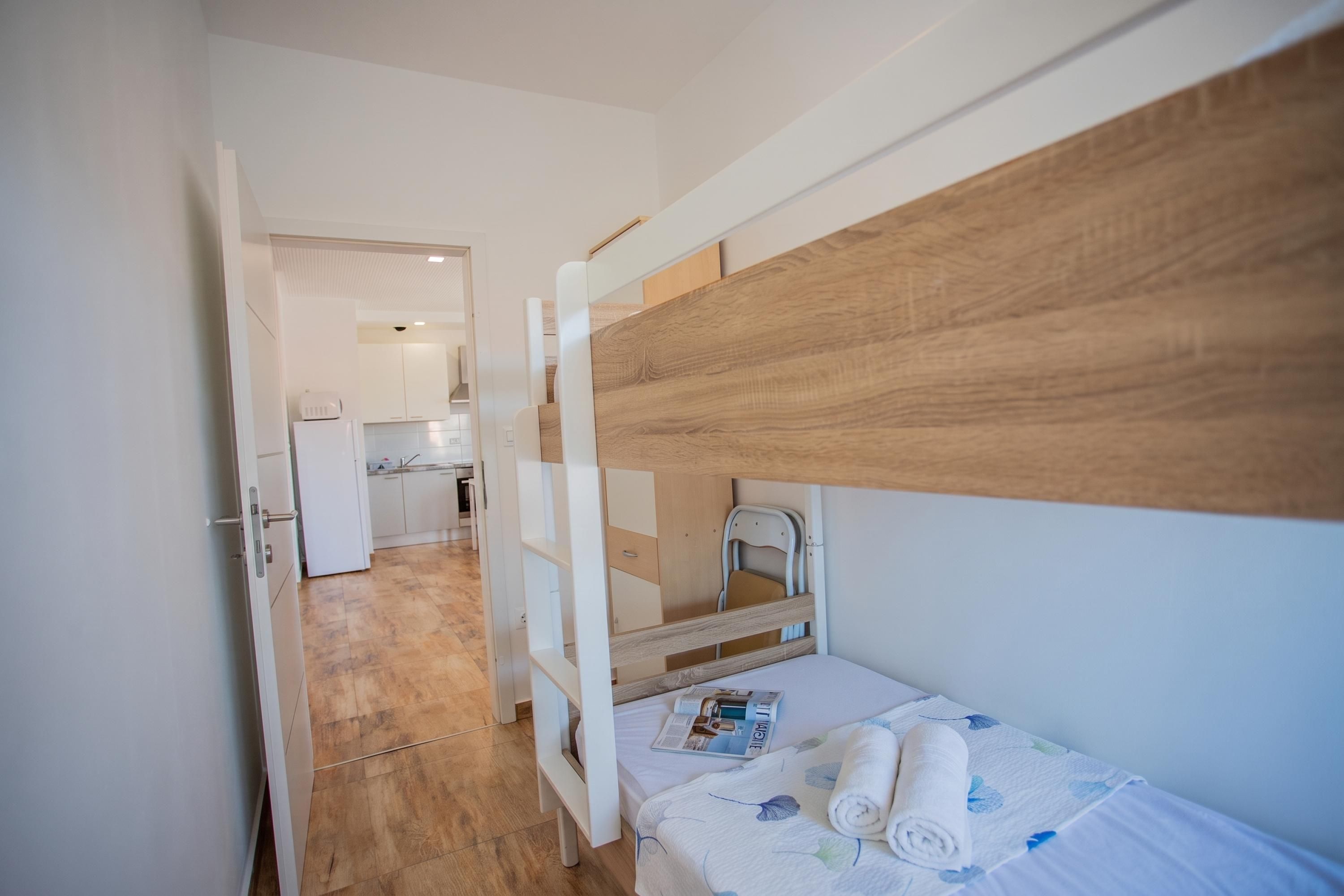 Quarto pequeno com beliche, cozinha compacta e porta para o banheiro.