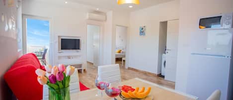 Una sala de estar moderna con un sofá rojo, una mesa de centro de vidrio y una disposición de frutas, además de un televisor montado en la pared.