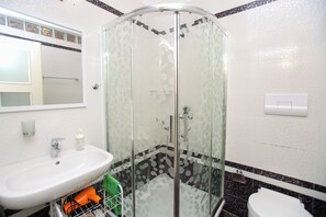 Ein Badezimmer mit einer Duschkabine, einem Waschbecken, einer Toilette und einem Spiegel.