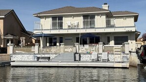 A two-story waterfront property with a dock, outdoor seating, and a clear sky. - Lakeside Paradise - Hot Tub, Dock, 5bdrm, Firepit (Victorville)