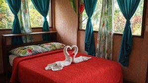 A bed with a red quilt, two white swan-shaped pillows, and teal curtains. - Ilan Ilan tortuguero (Colorado)