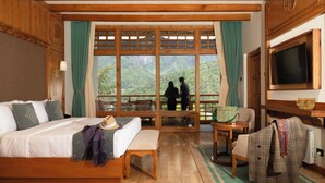 A hotel room with a bed, a desk, a chair, and a large window offering a mountain view. - Amba Paro (Paro)