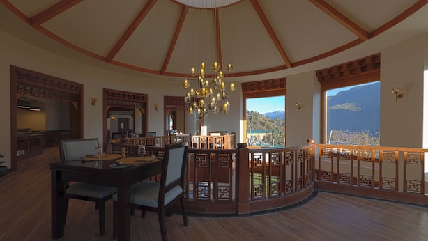 A spacious dining area with a high ceiling, a chandelier, and a view of mountains through large windows. - Amba Paro (Paro)