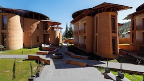 A courtyard with buildings featuring curved walls and wooden balconies, surrounded by a paved walkway and small planters. - Amba Paro (Paro)