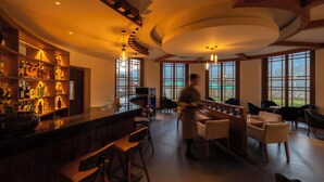 A bar area with a counter, stools, and shelves of bottles. There are large windows with a view of the outdoors. - Amba Paro (Paro)
