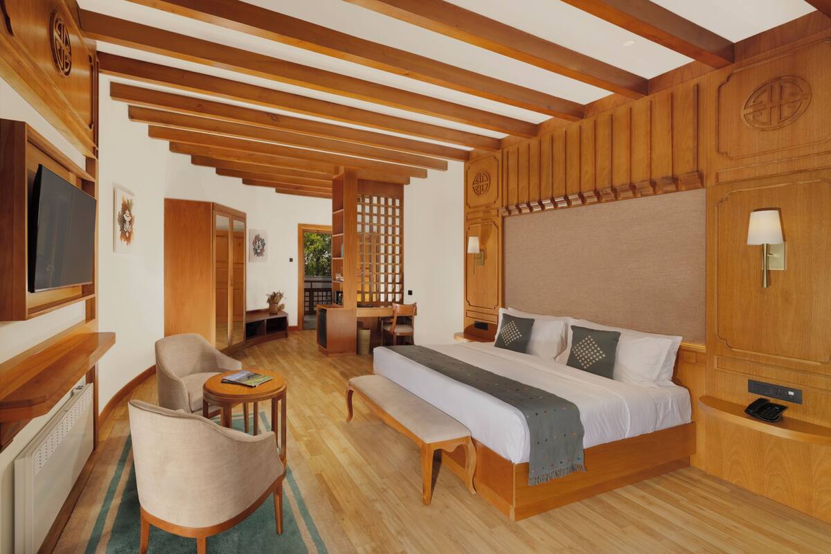 Quarto de hotel com teto de madeira, uma cama grande, uma escrivaninha, uma cadeira e uma televisão.