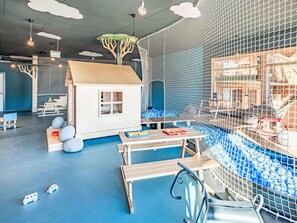 Ein Spielbereich mit einem Netzabschirmung, einem kleinen Holzhaus und einem Tisch mit Spielzeug.