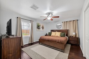 A bedroom with a bed, a ceiling fan, a TV, a desk, and a window with curtains. - Houston Parkside Haven Near Med Center and UH (Houston)