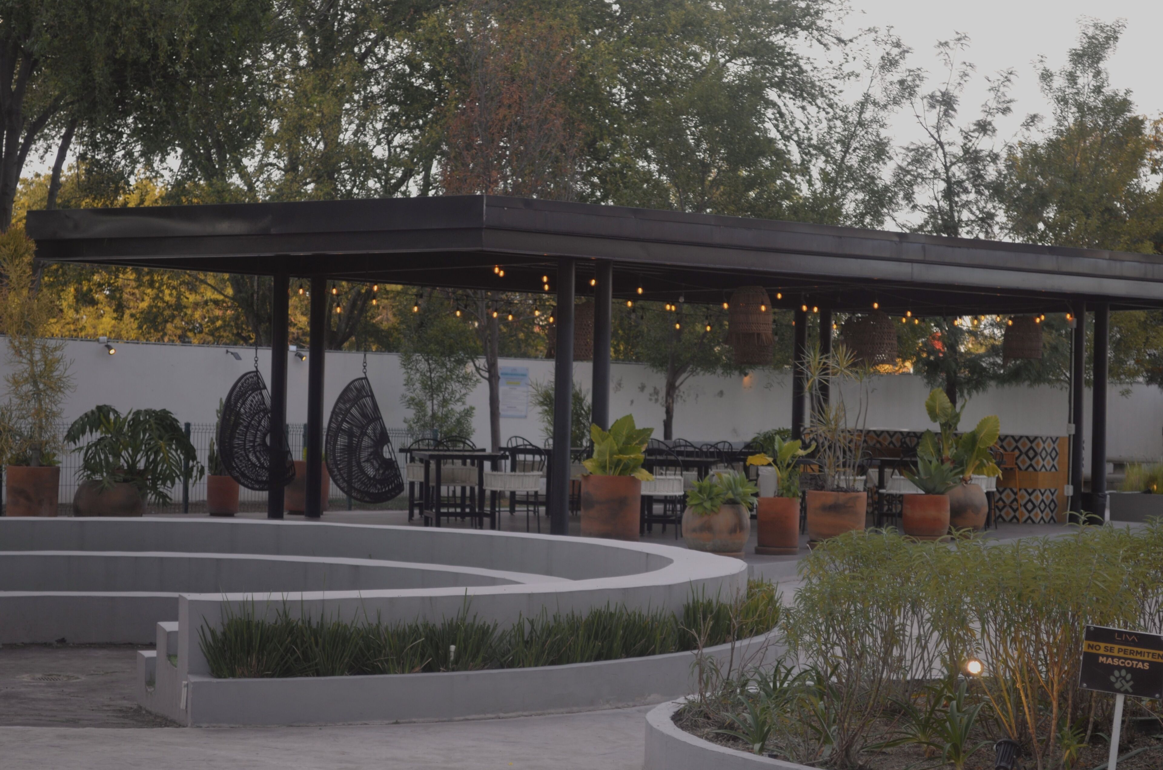 A covered outdoor seating area with tables and chairs, surrounded by planters and a decorative wall.
