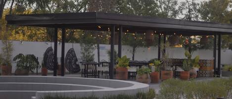A covered outdoor seating area with tables and chairs, surrounded by planters and a decorative wall.