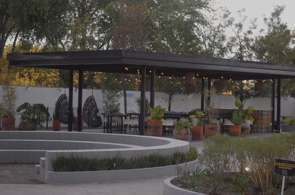 Un espace extérieur abrité, aménagé avec des tables et des chaises, entouré de jardinières et agrémenté d’un mur décoratif.