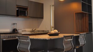 Una cocina moderna con una isla central, taburetes de bar, microondas y licuadora.