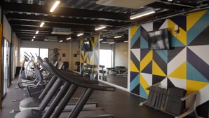 Un gimnasio con cintas de correr, equipo de ejercicio y un llamativo diseño de pared con formas geométricas.