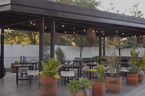 An outdoor patio with tables and chairs, potted plants, and hanging lights. - LIVA Departamento 2 Recámaras y Alberca  (Zapopan)