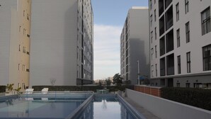 Una piscina con sillones de descanso, rodeada de edificios modernos con balcones.