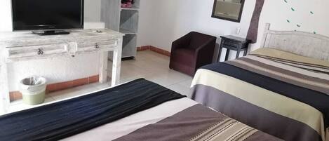 Una habitación de hotel con cama, televisor, cómoda, sillón y armario.