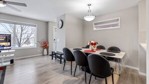 Un coin repas comprenant une table, des chaises, un ventilateur de plafond, une horloge et une fenêtre donnant sur un paysage agréable.