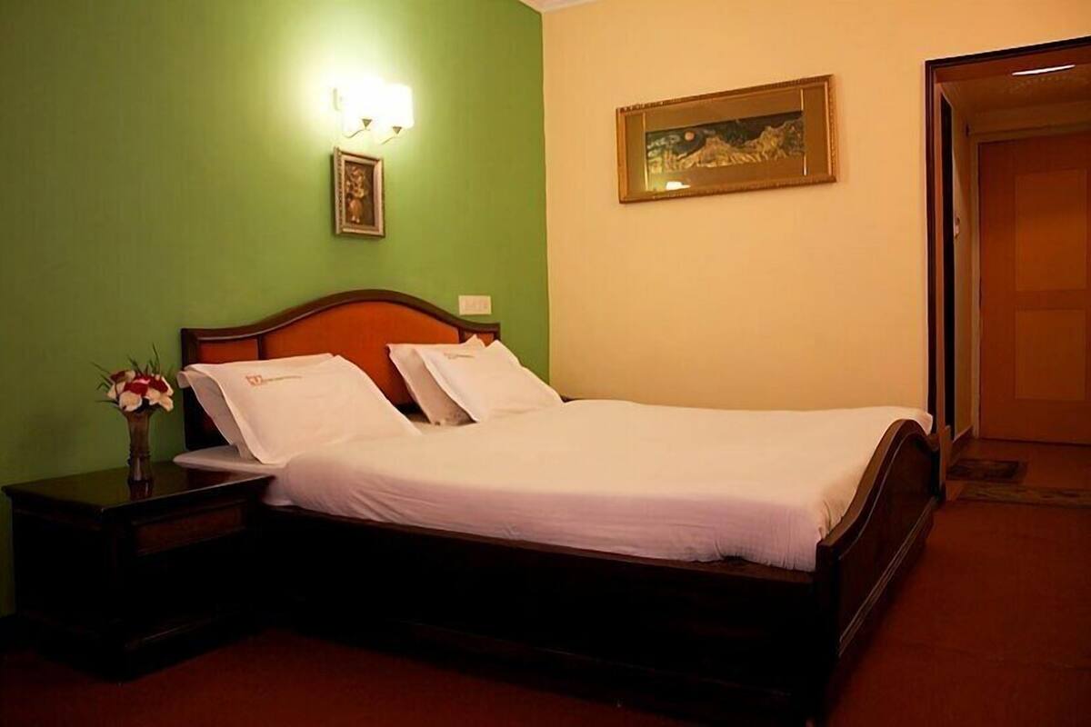 A neatly made bed with white linens, a wooden headboard, a nightstand with a vase of flowers, and a framed picture on the wall.