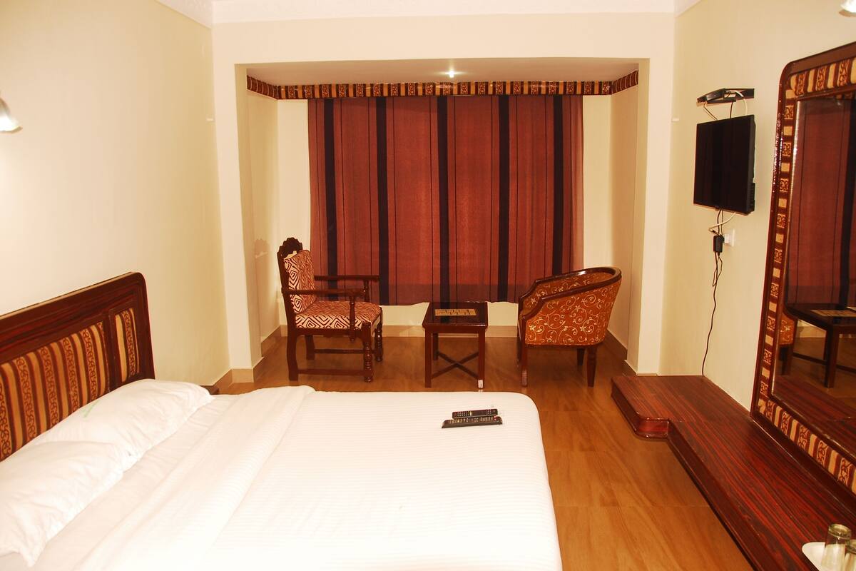 A hotel room with a bed, two chairs, a small table, a TV, and a mirror.