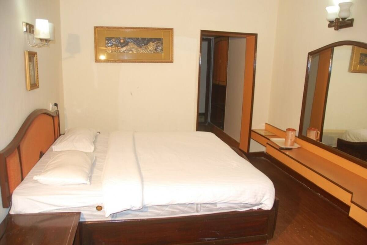 A hotel room with a bed, a bedside table, a mirror, and a framed picture on the wall.