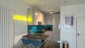 A modern kitchen with a neon sign, a dining area with bar stools, and a small trash bin.