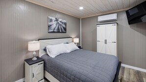 Une chambre à coucher avec un lit, des tables de chevet, une télévision et une armoire.