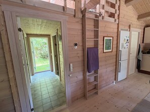 A wooden interior with a hallway leading to a door, a shelf with a towel, and a refrigerator. - Traditional log house near beach and forest (Rørvig)