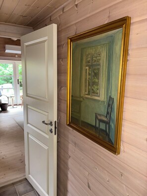 Une pièce avec un mur lambrissé en bois, une porte dotée d’une poignée en laiton et un tableau représentant une pièce avec une fenêtre et une chaise.