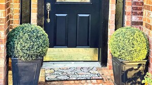 A black door with a welcome mat, two potted plants, and a brick wall. - Newly renovated 3 bedroom house near Allen premium outlets (Allen)