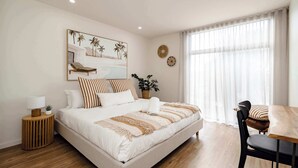 Un dormitorio con cama, mesita de noche, lámpara y una ventana con cortinas.
