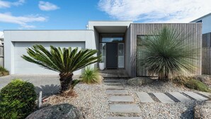Una casa moderna con camino de grava, una palmera y un sendero que lleva a la entrada.