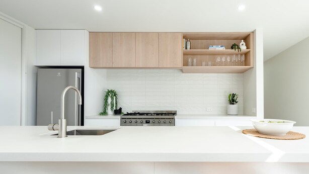 Una cocina moderna con un refrigerador de acero inoxidable, estufa a gas, alacenas blancas y una repisa de madera con cristalería.