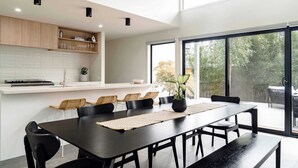 Una cocina moderna con armarios blancos, un comedor con mesa negra y un ventanal con vistas a árboles.