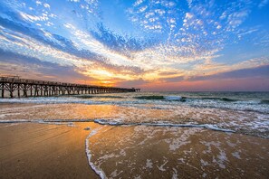Ein Strand mit Wellen, einer Seebrücke und einem Sonnenuntergang.