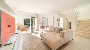 Ein modernes Wohnzimmer mit einer Couch, einem Fernseher, einem Glastisch und Blick ins Freie.