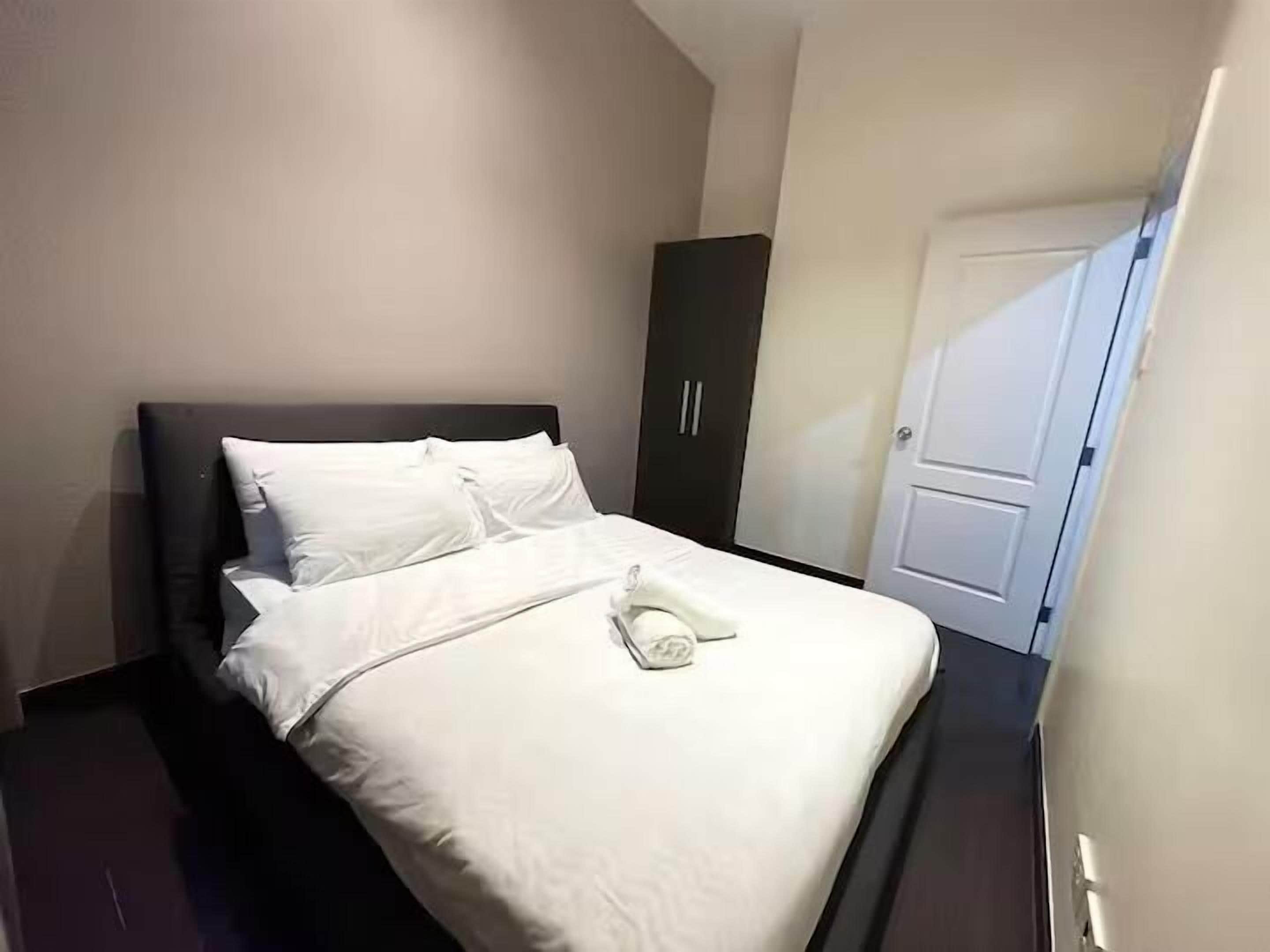 A neatly made bed with white linens, a dark headboard, and a white door to the right.