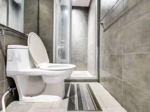 Een moderne badkamer met toilet, douche en een douchecabine met glazen wanden.