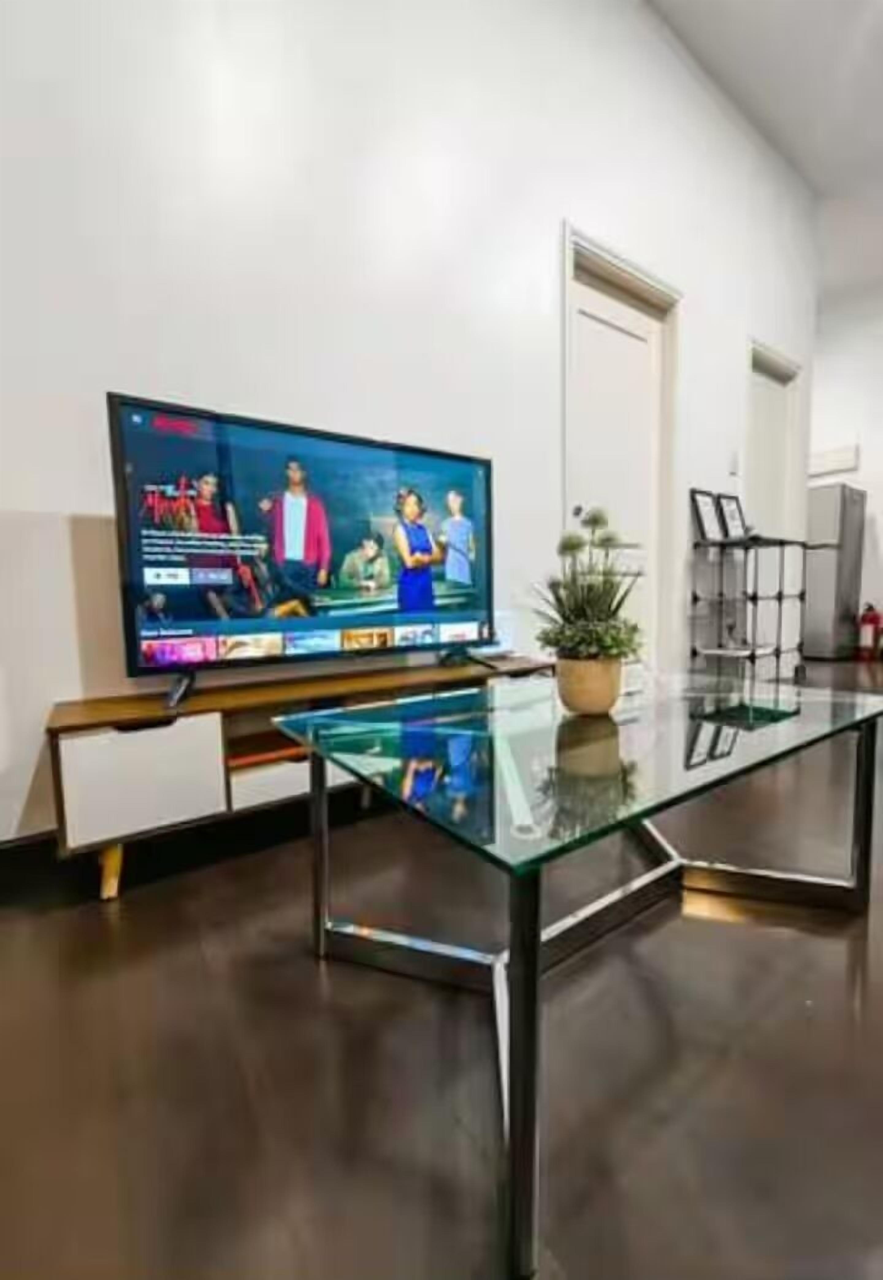 A modern living room with a flat-screen TV, a glass coffee table, and a potted plant.
