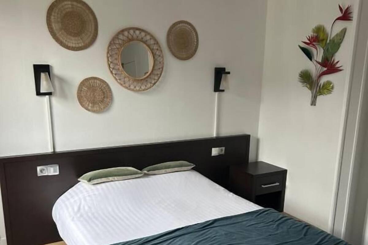 A neatly made bed with a white and teal bedspread, a dark headboard, and a wall-mounted mirror.