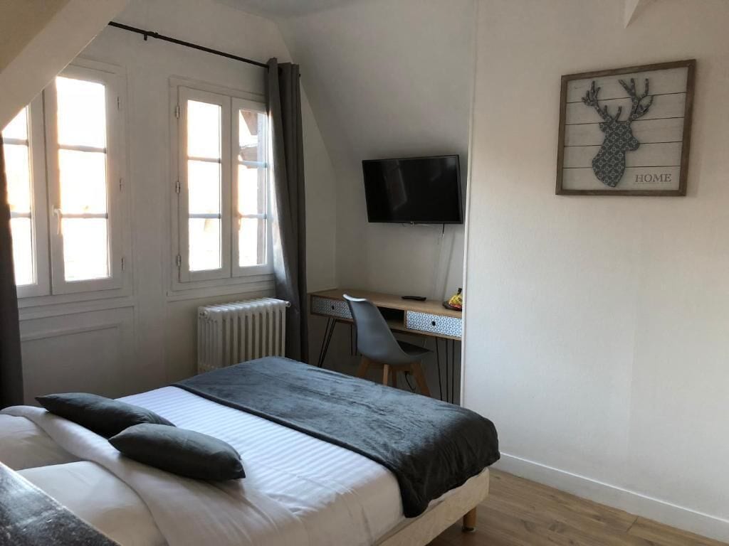 A bedroom with a bed, a desk, a chair, a television, and a deer head decoration on the wall.