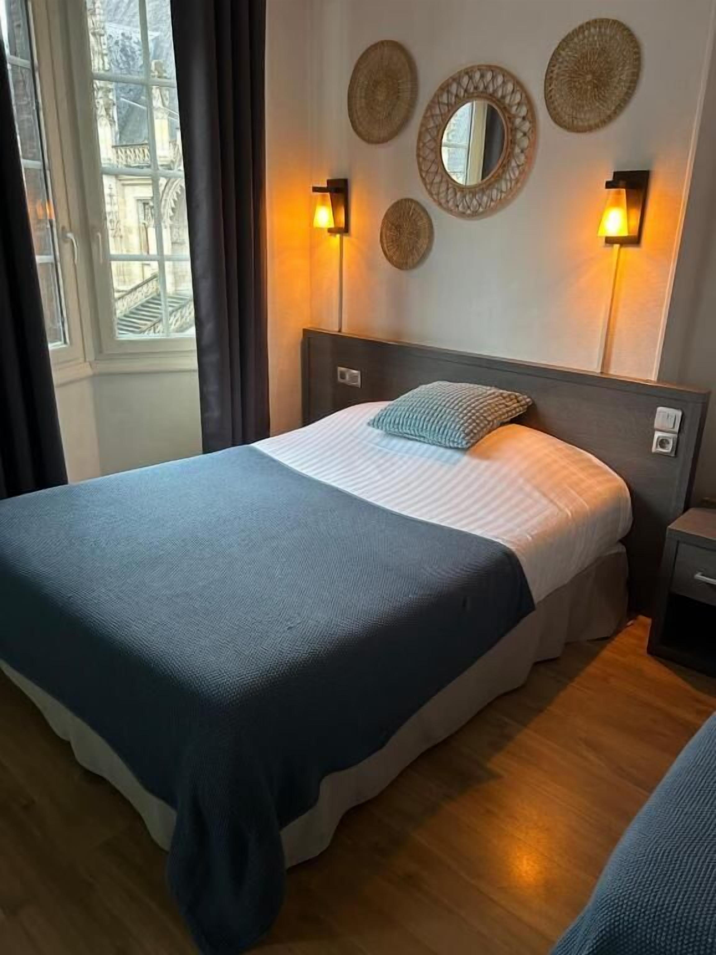 Habitación de hotel con cama, dos lámparas fijadas a la pared y una ventana con cortinas.