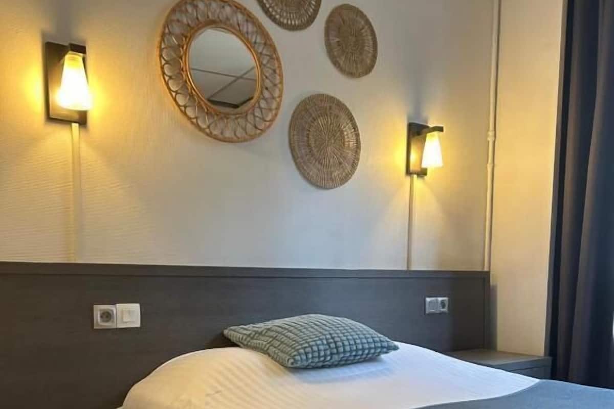 A hotel room with a bed, wall-mounted lights, and decorative wall art.