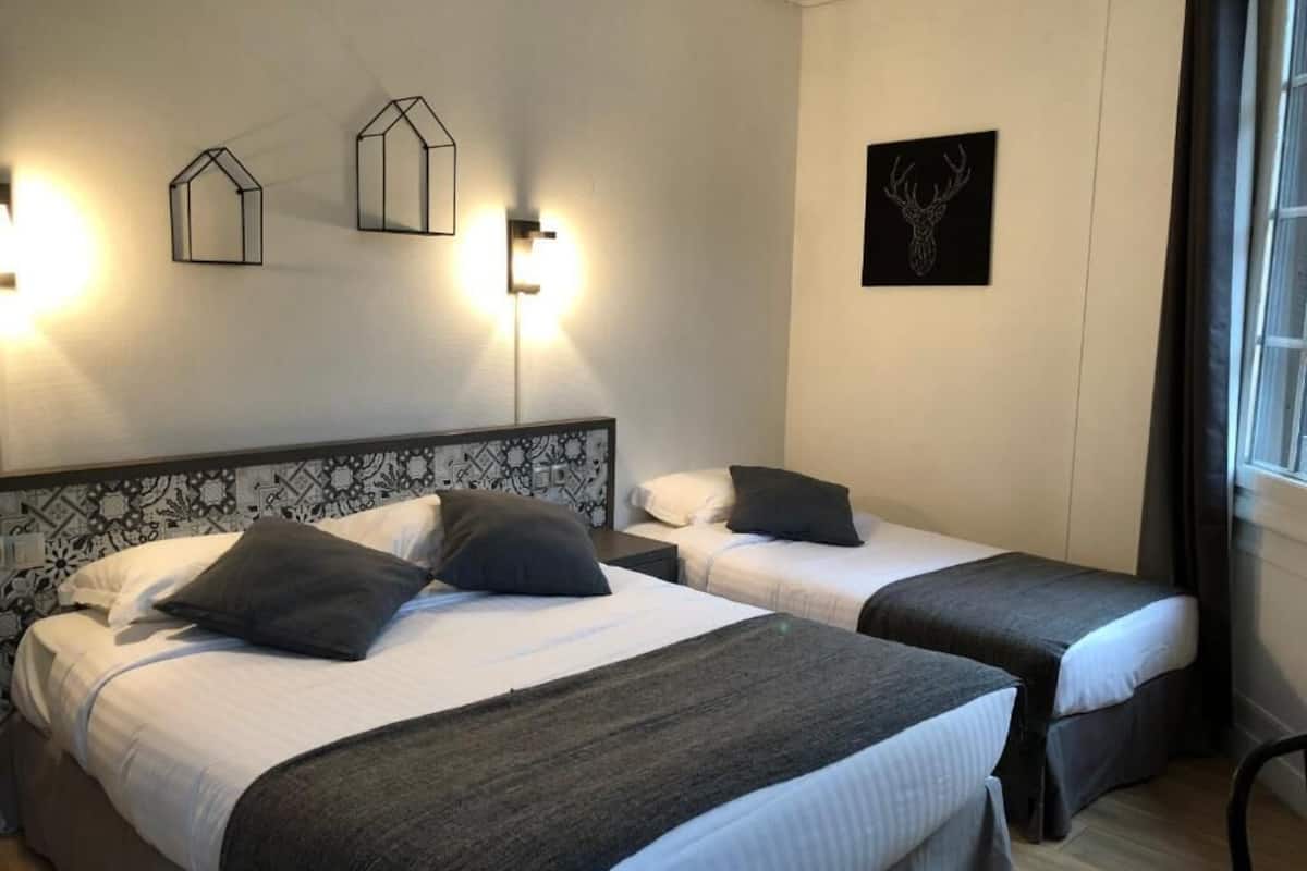 A hotel room with two beds, a patterned headboard, wall-mounted light fixtures, and a deer head artwork.