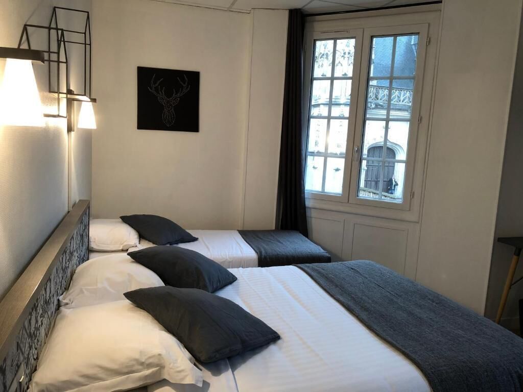 A bedroom with two beds, a window with a view, and a wall-mounted light fixture.