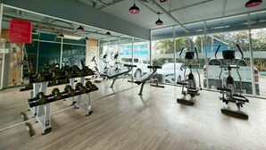 A gym with exercise equipment, large windows, and a view of parked cars outside. - Sea Dream Jomtien Beach (Pattaya)
