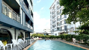 A swimming pool with lounge chairs, a covered area, and a multi-story building with balconies. - Sea Dream Jomtien Beach (Pattaya)
